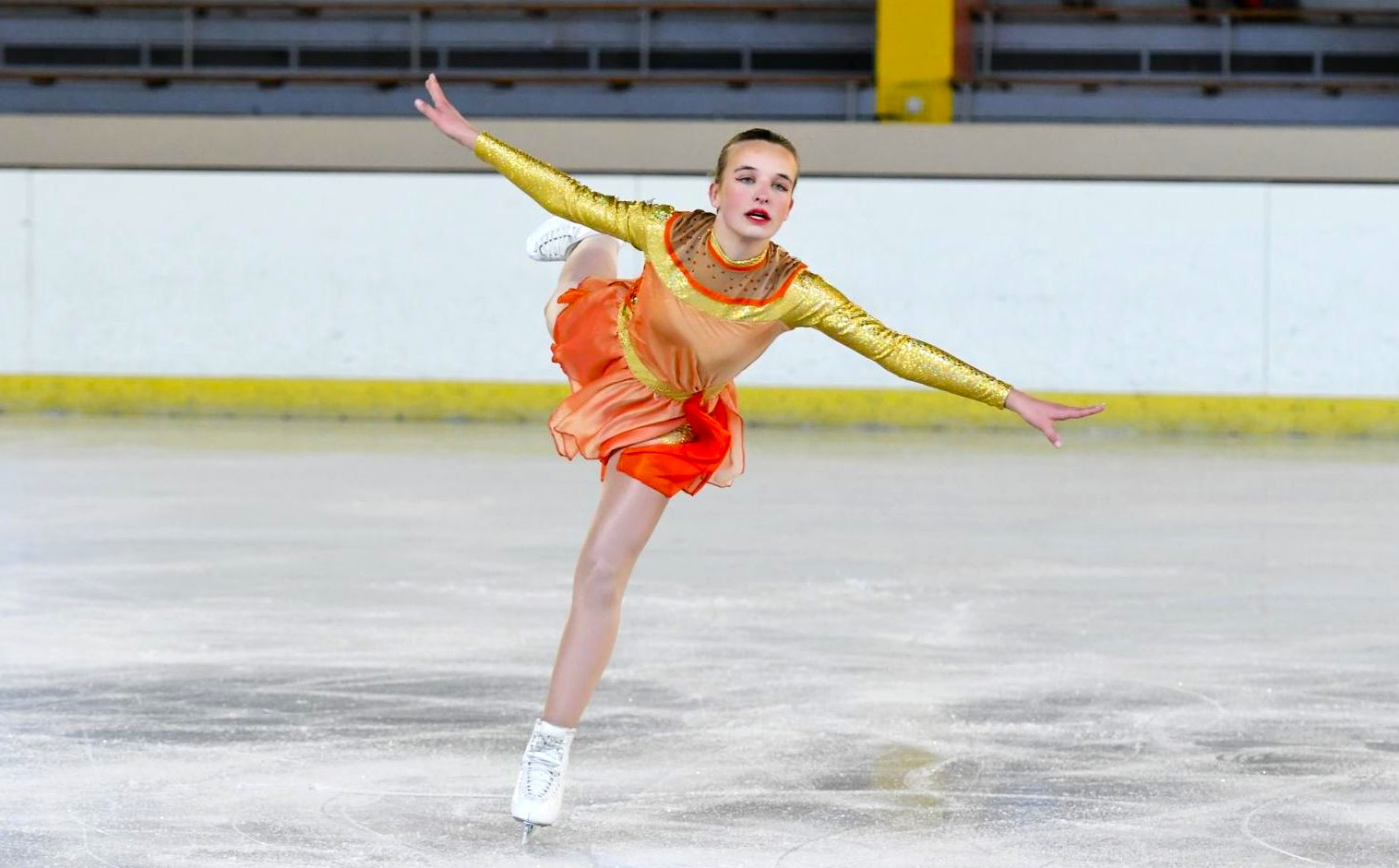 Patineuse en tenue orange réalisant une arabesque