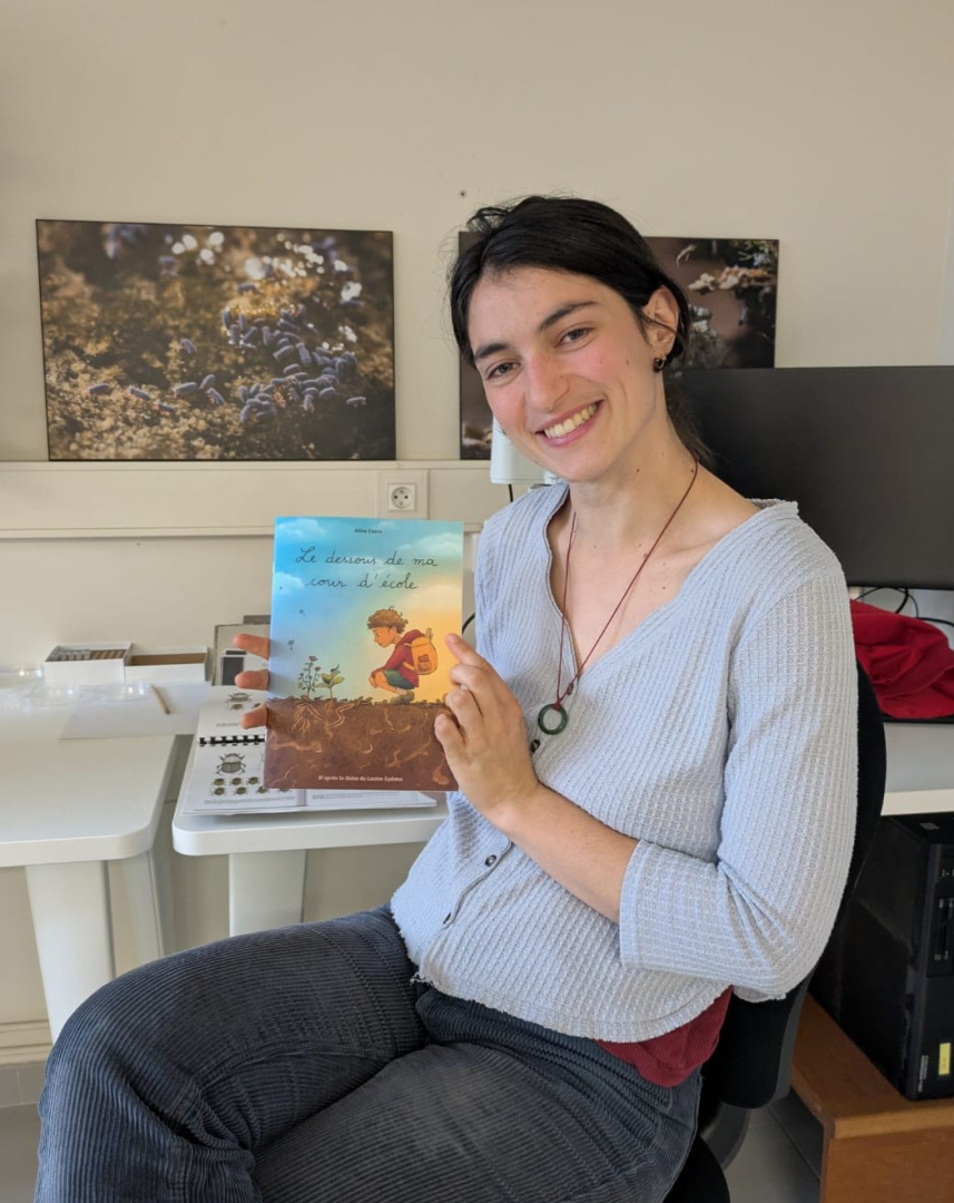 La post-doctorante Louise Eydoux pose avec la BD illustrant sa thèse, photos et ordinateur en arrière-plan